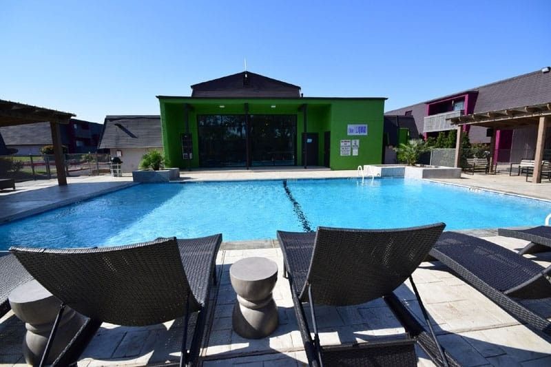 Modern poolside lounge with blue swimming pool, green building, and black chairs under a clear sky