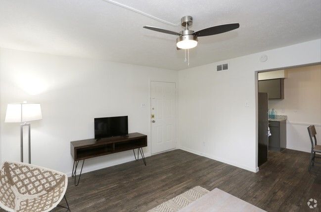 Empty living room with ceiling fan, TV on console, floor lamp, and open doorway to kitchen