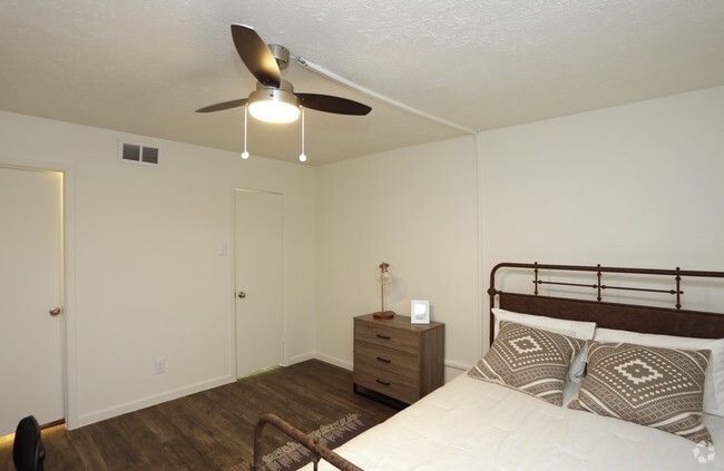 Minimal bedroom with white walls, ceiling fan, bed, dresser, and closed doors on wood flooring