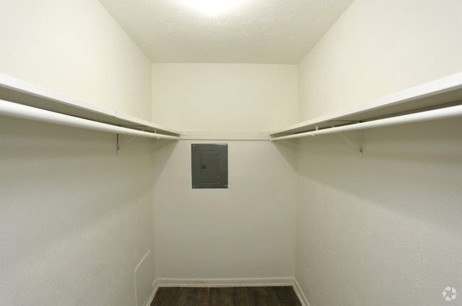 Empty white walk-in closet with shelves on both sides and a small panel on the back wall.