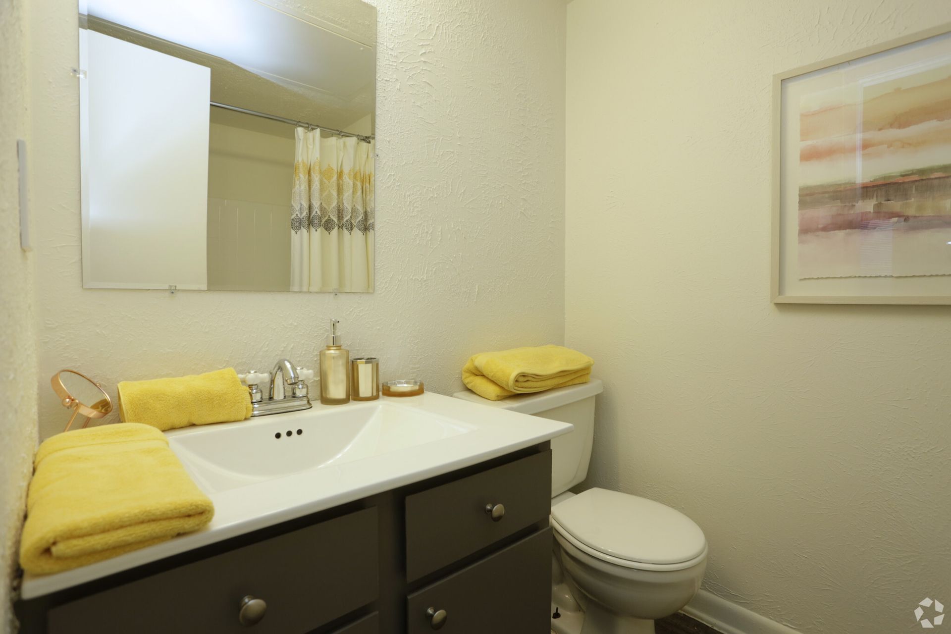 Small bathroom with a sink, mirror, toilet, and yellow towels on a white counter.