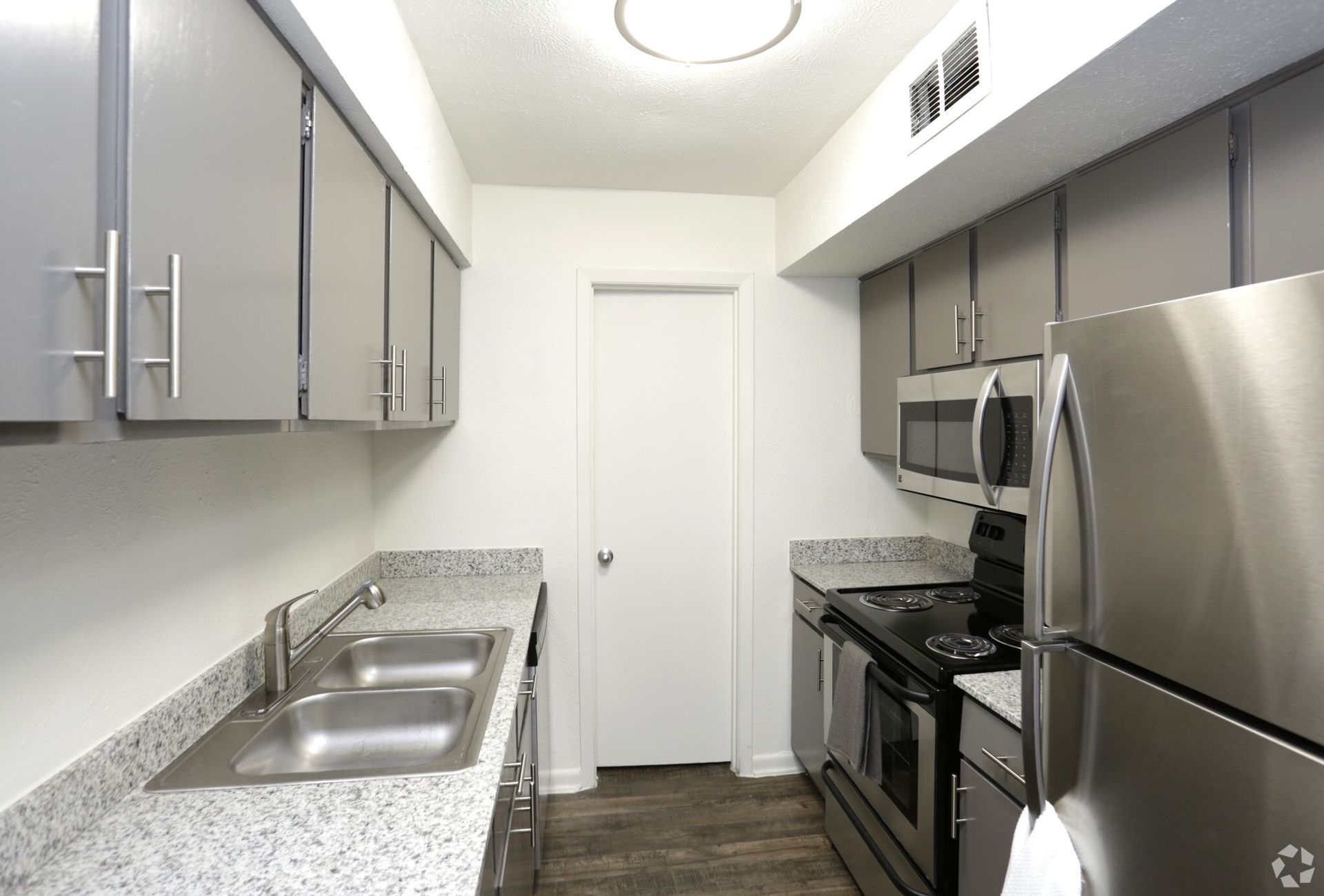 Compact galley kitchen with gray cabinets, granite counters, stainless appliances, and a double sink.