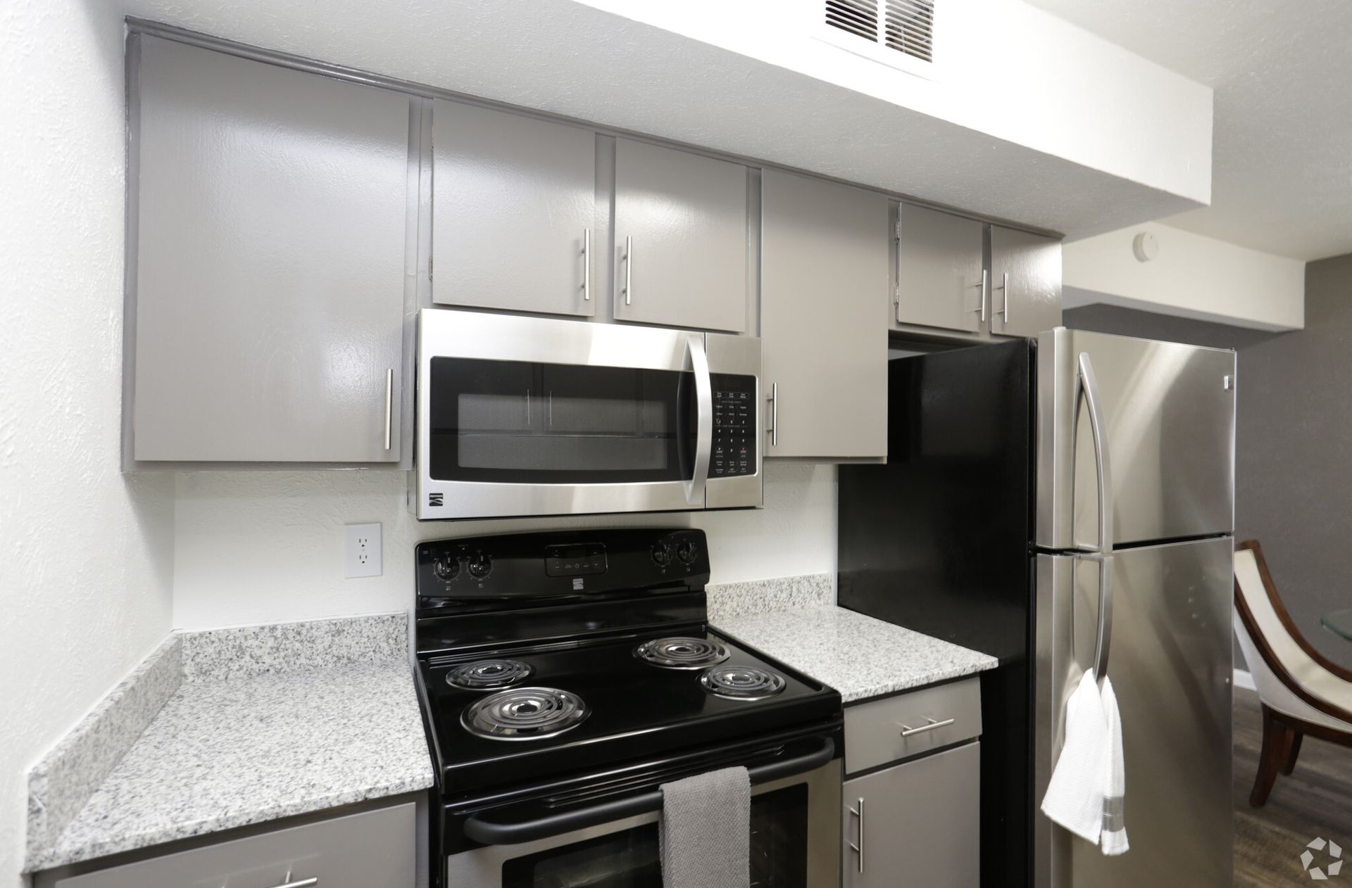 Compact kitchen with gray cabinets, black stove, microwave, and stainless steel refrigerator