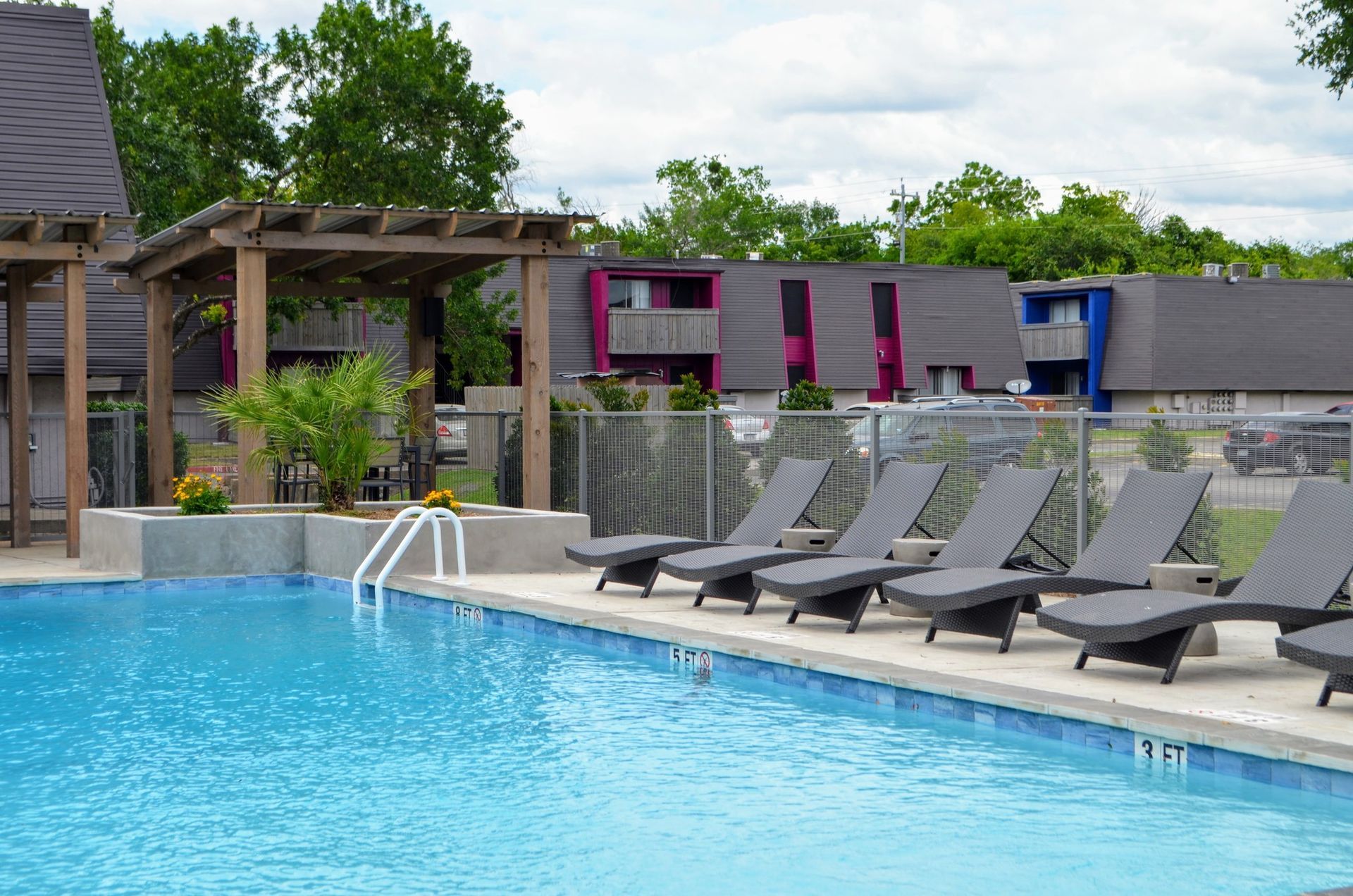 Outdoor pool with lounge chairs, pergola, and modern building in the background