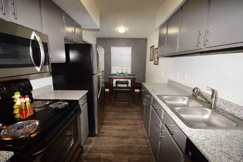 Narrow modern kitchen with black appliances, gray cabinets, and a small dining table by the window