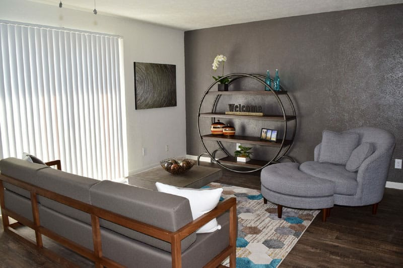 Modern living room with gray sofa, round chair, wall shelf, rug, and sliding blinds