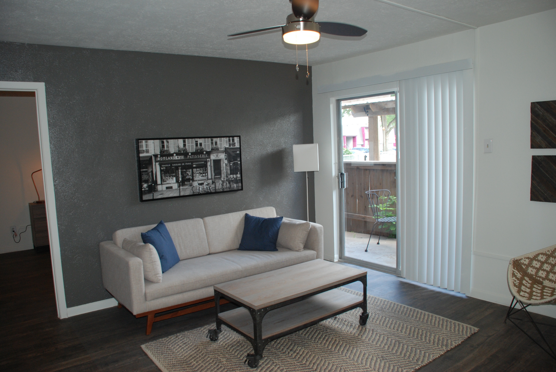 Modern living room with beige sofa, blue pillows, coffee table, wall art, and sliding glass doors to a patio.