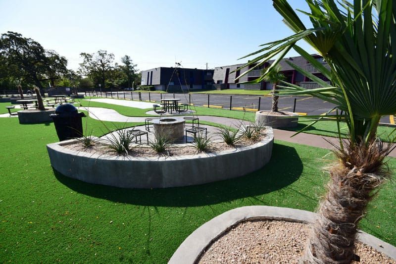 Landscaped courtyard with artificial turf, circular planters, and a small fountain near buildings