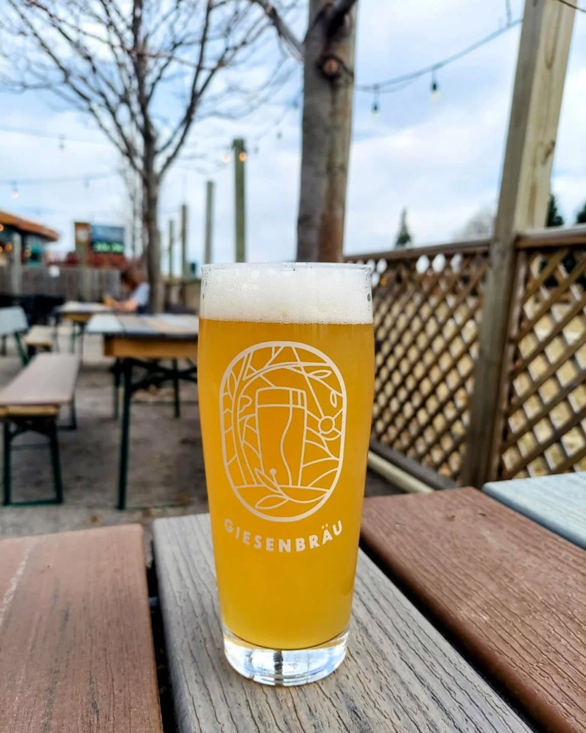 A glass of amber beer on a patio table with outdoor seating in the background.