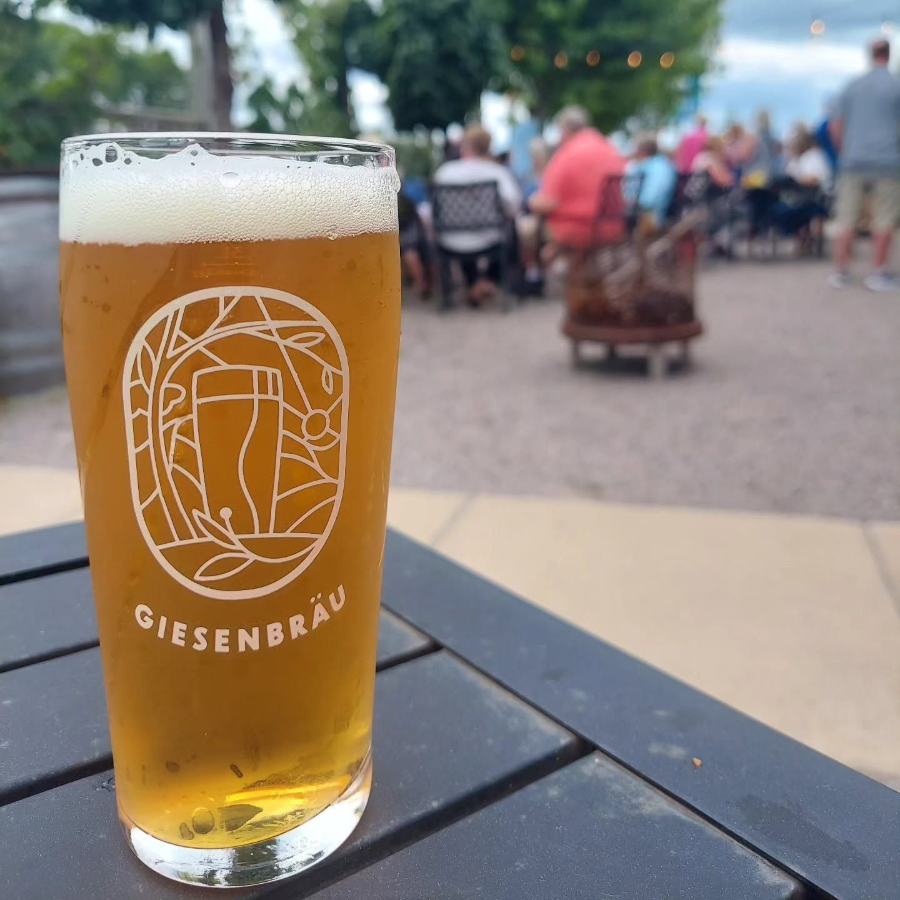Pint of beer on a table at an outdoor gathering, with people and trees blurred in the background