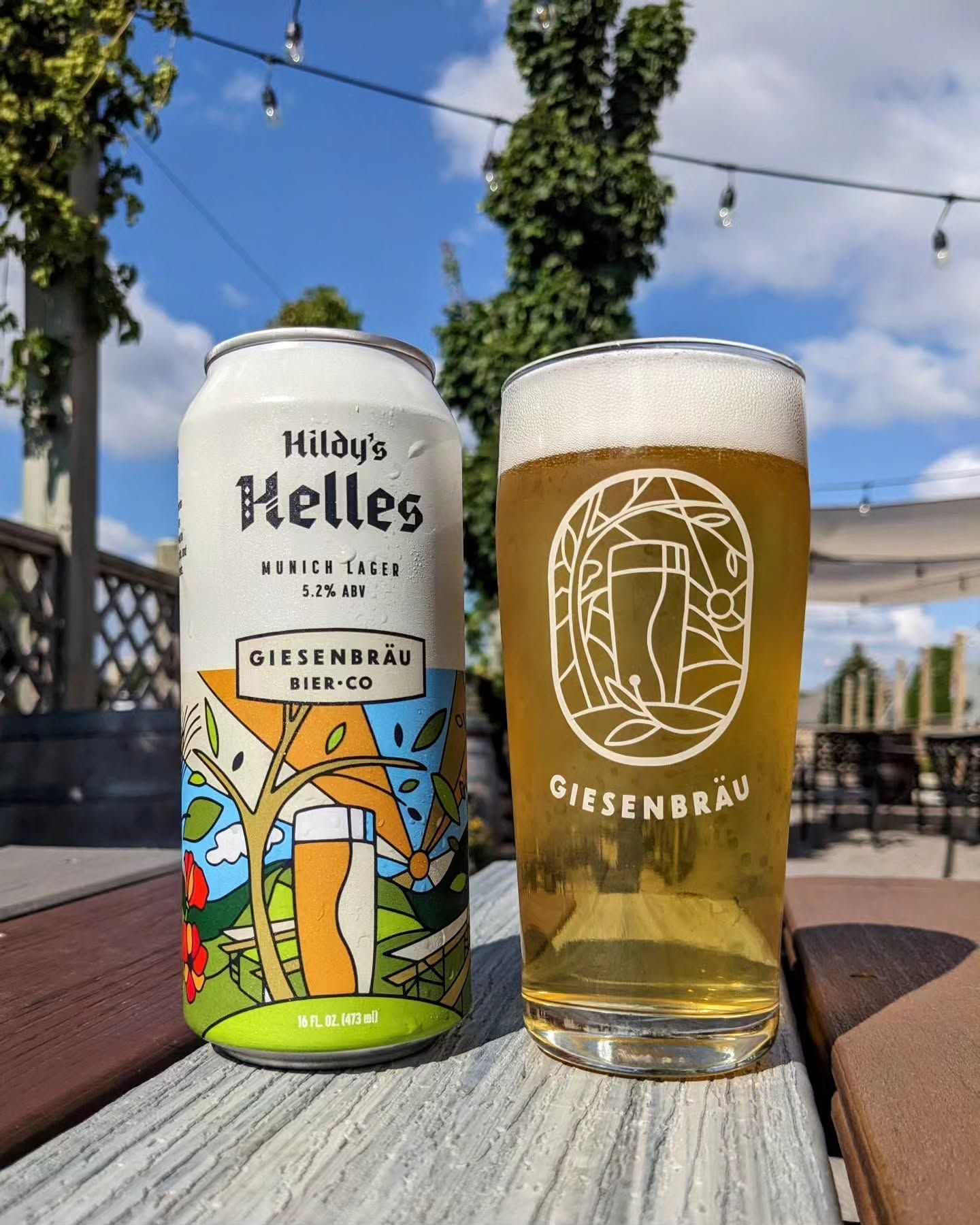 Glass of beer and Helles can on a wooden table outdoors in a sunny park.