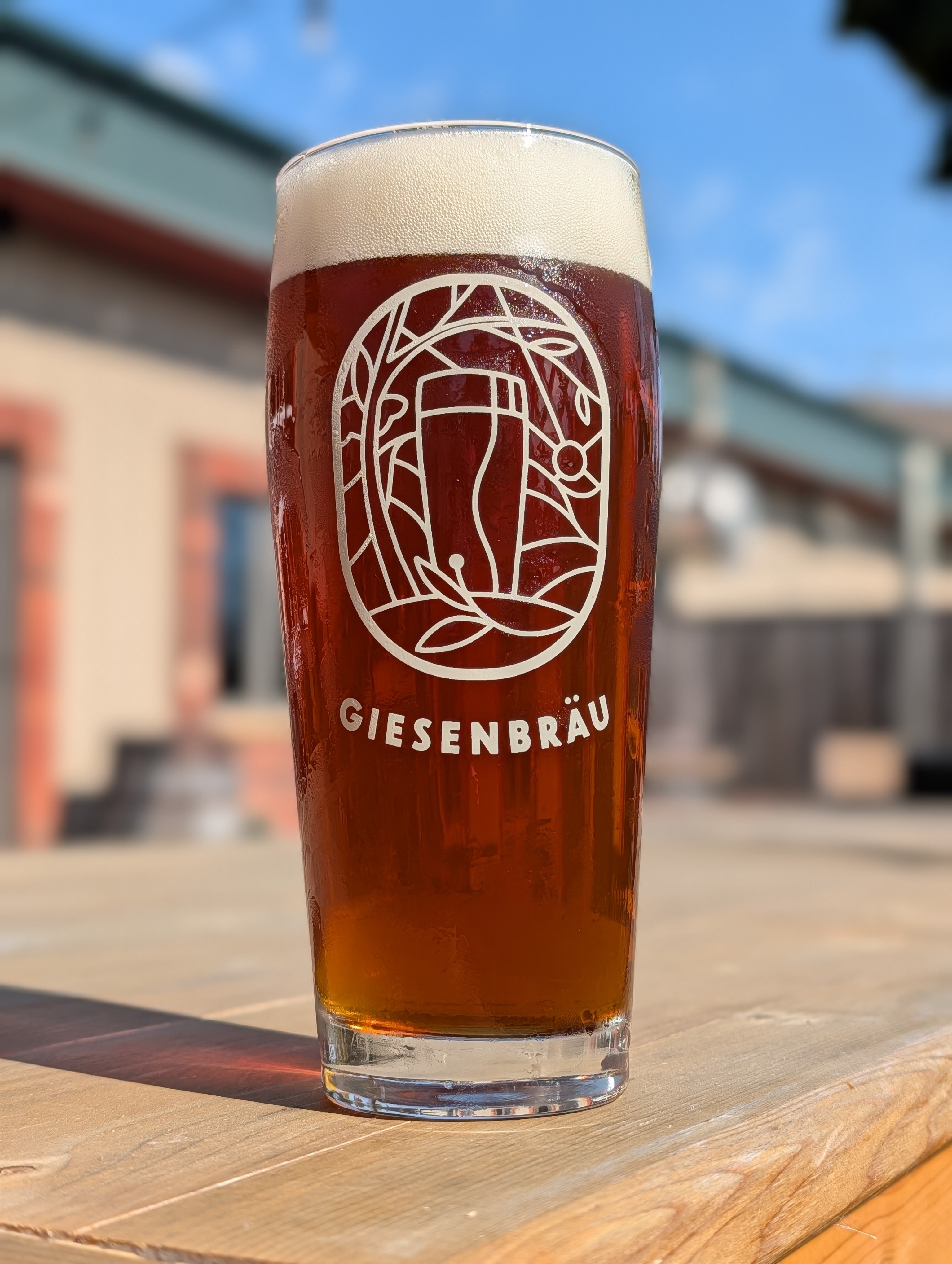 Tall glass of amber beer with foam on an outdoor café table, branded