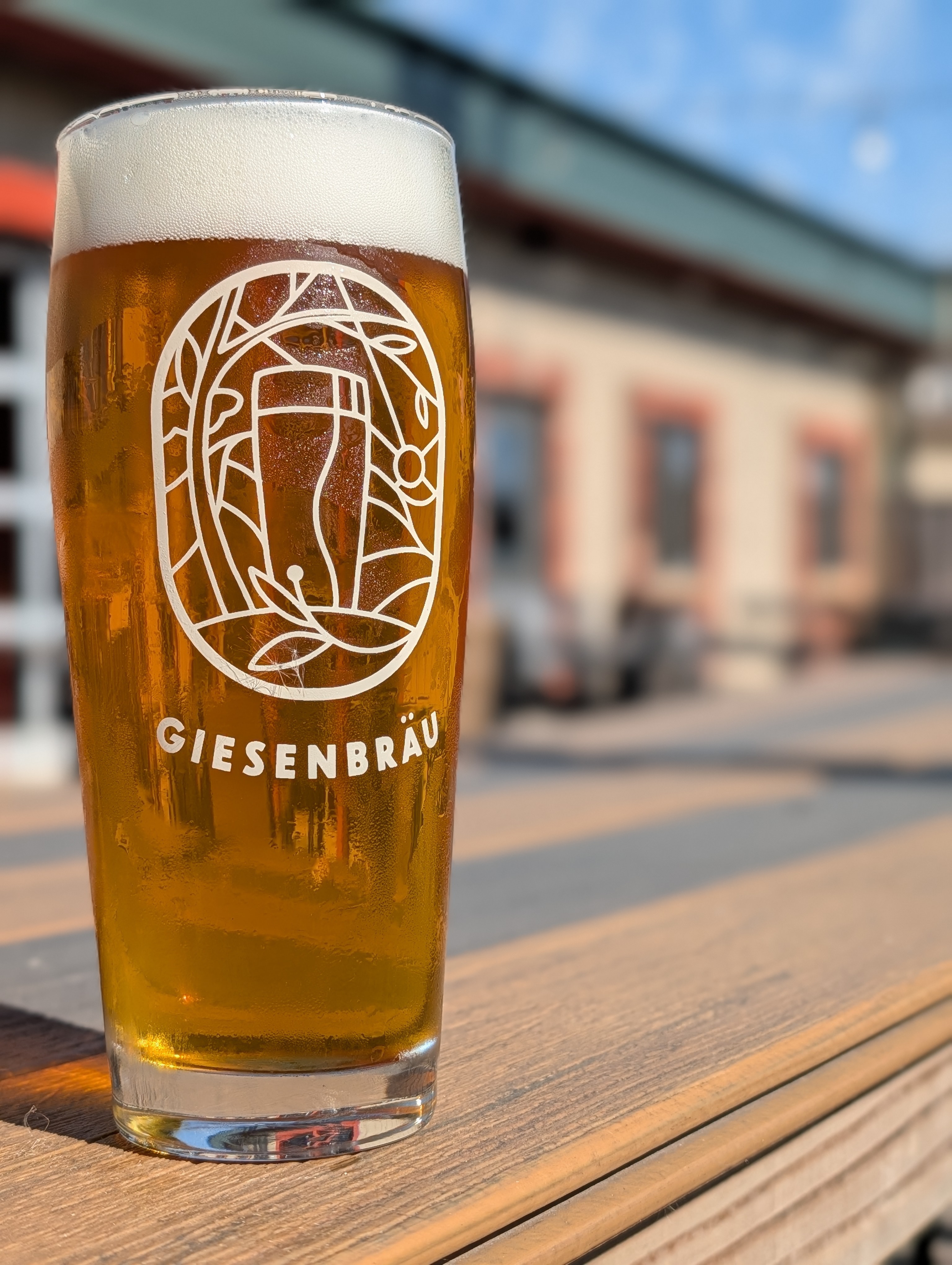 Pint of amber beer with foam on an outdoor patio in sunlight