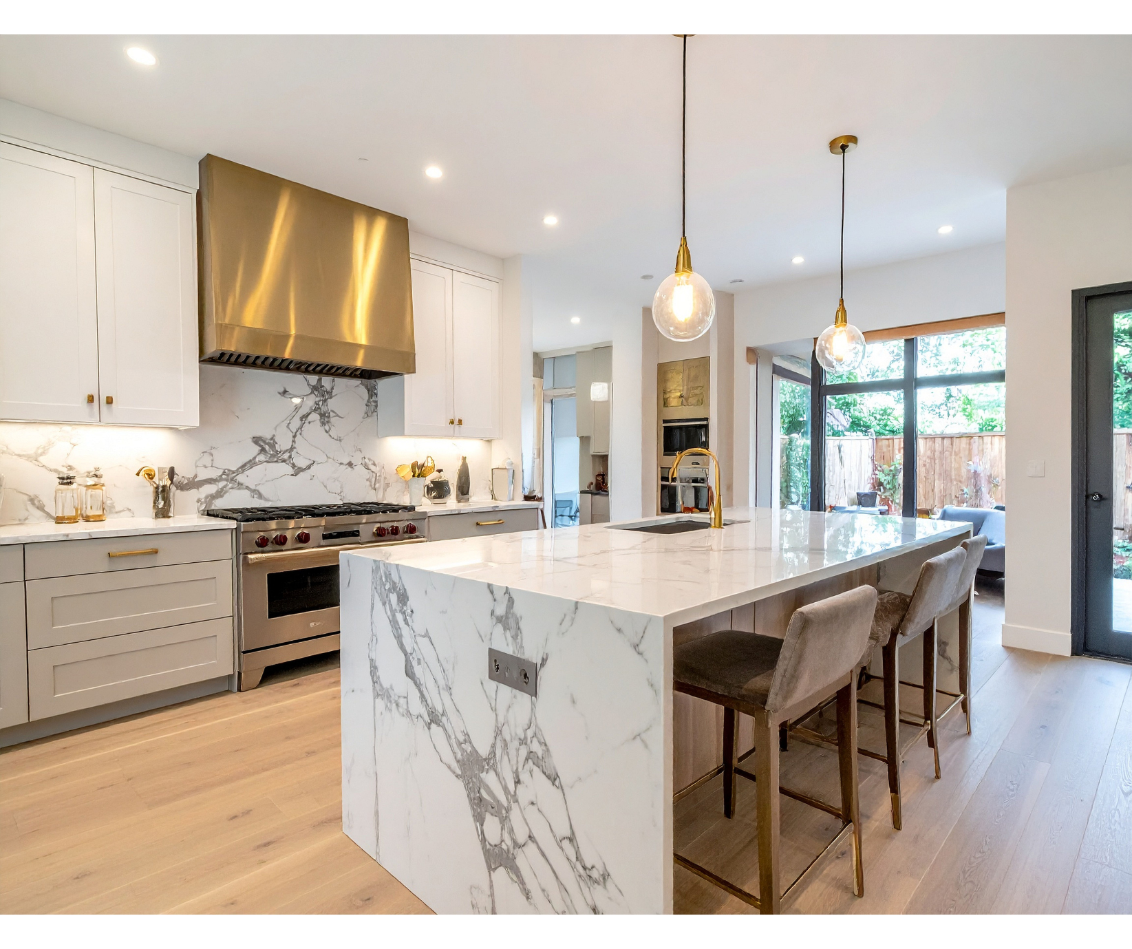 Modern kitchen with marble island and countertops, stainless steel appliances, and gold accents.