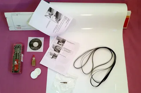 White roll of material with instructions, cords, and small tools on a pink background