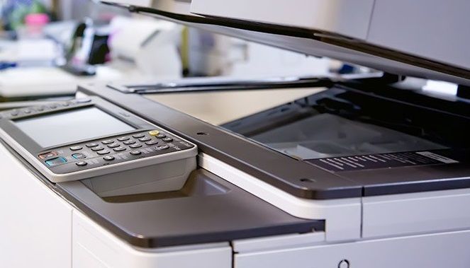 Black-and-silver office printer with scanner lid open, viewed close up on a desk.