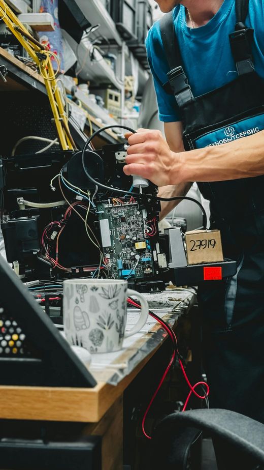 Technician working inside a laptop repair setup with exposed wires and tools on a cluttered workbench