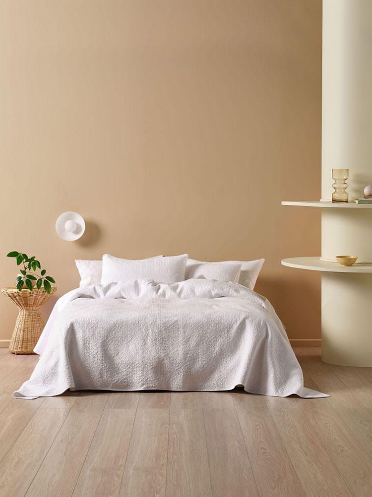 Bedroom with white bed, beige walls, wooden floor, and side table with plant.