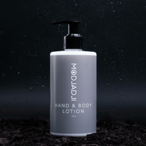 Gray bottle of Modjadji hand and body lotion with black pump, on dark ground against a black background.