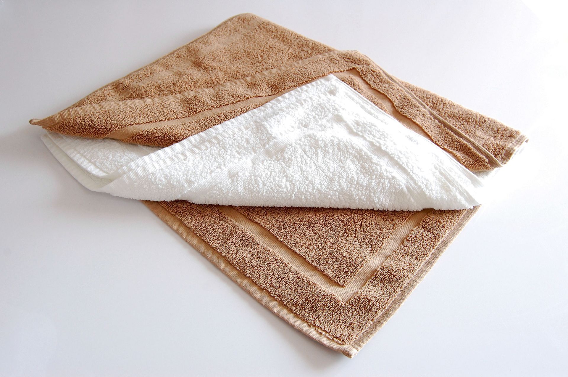 Two towels folded, a brown one on top and a white one peeking out.