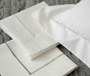 White bedsheets with gray trim, stacked on a gray knitted blanket.