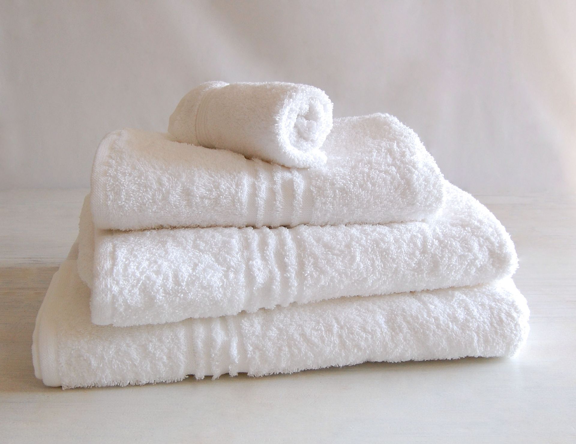 Stack of clean, white towels, one rolled on top.