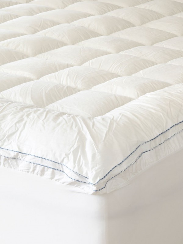 White, quilted mattress topper on a bed, close up showing the detail of stitching.