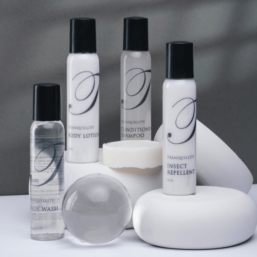 Hotel toiletries displayed on white platforms: body wash, lotion, shampoo, insect repellent, and soap.