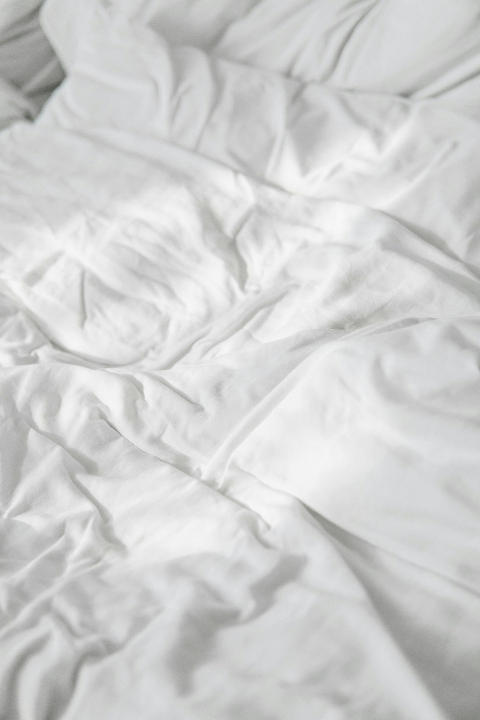 Wrinkled white bedsheets, unmade.