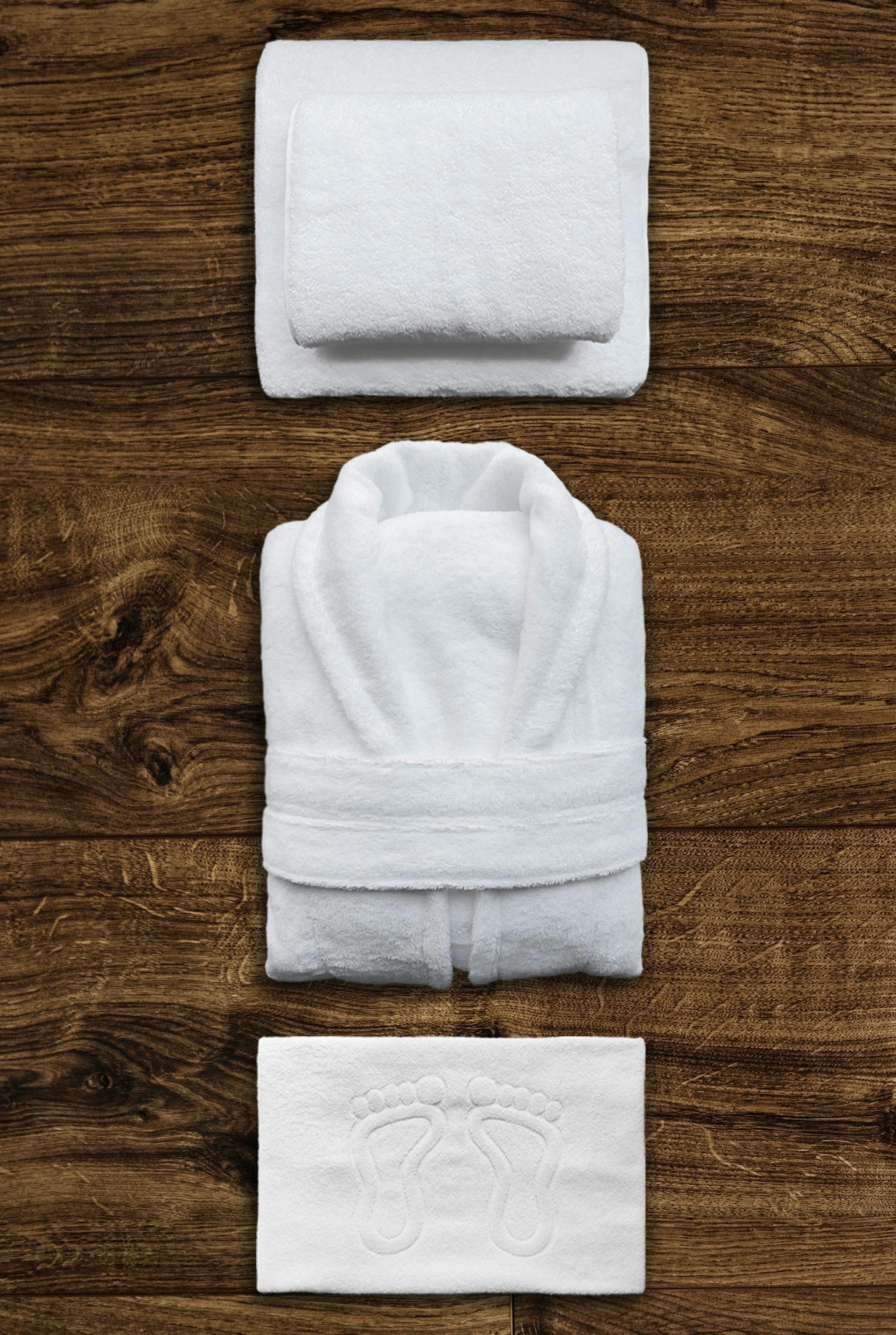 White folded towels, bathrobe, and washcloth on a dark wood surface.