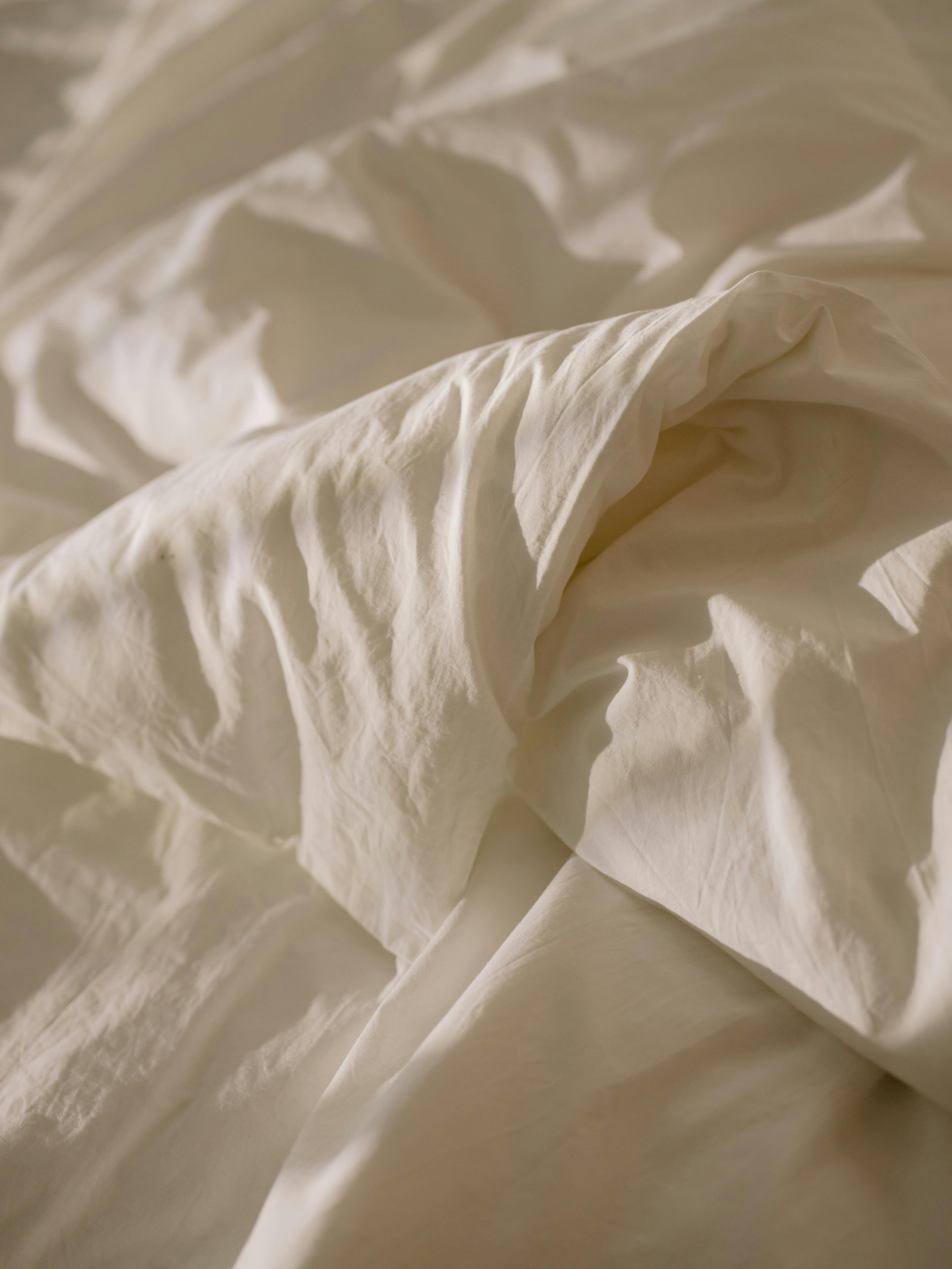 Wrinkled white bed sheets, partially illuminated by soft light.