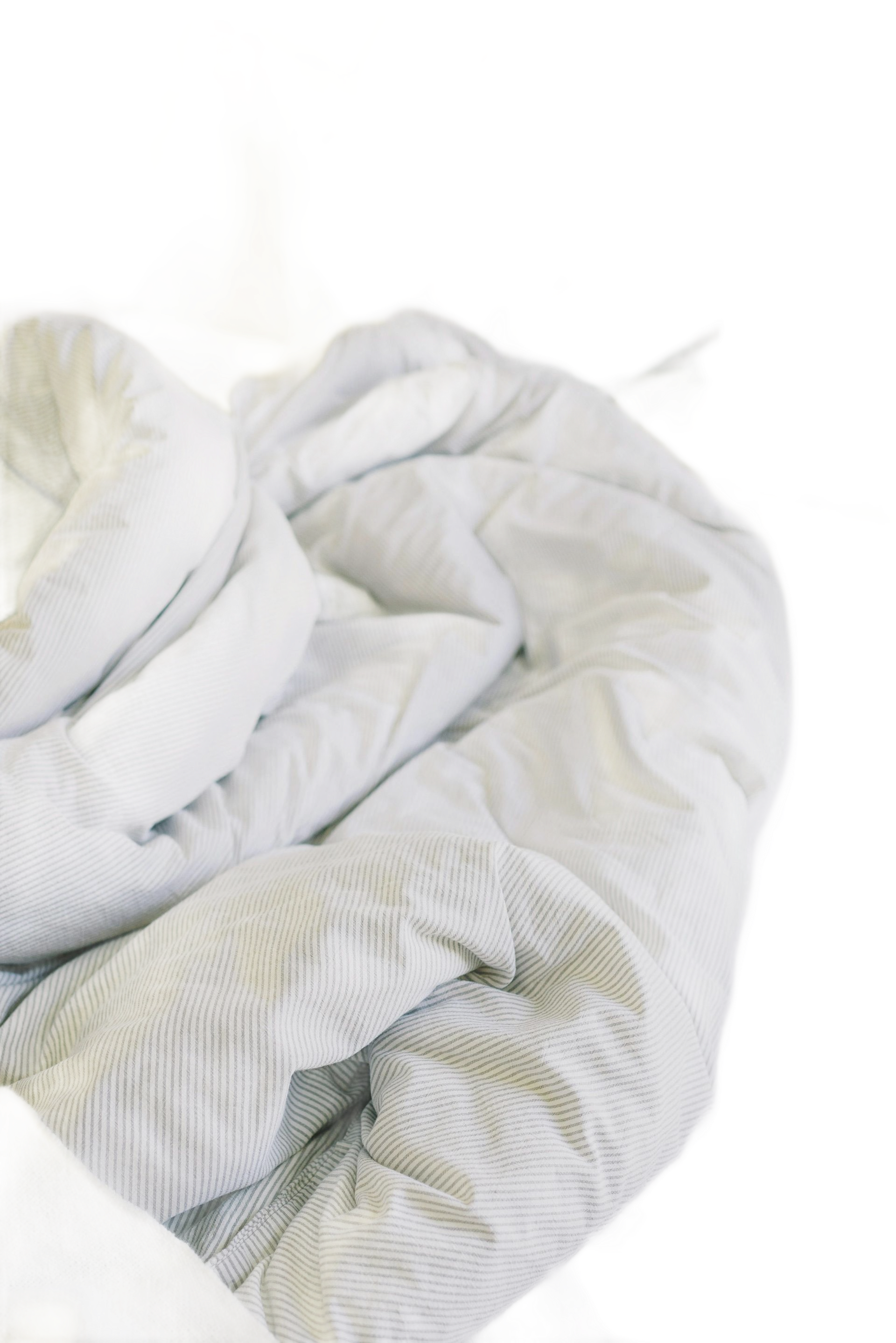 Unmade bed with white sheets, pillows, and a patterned duvet, creating a rumpled, cozy appearance.