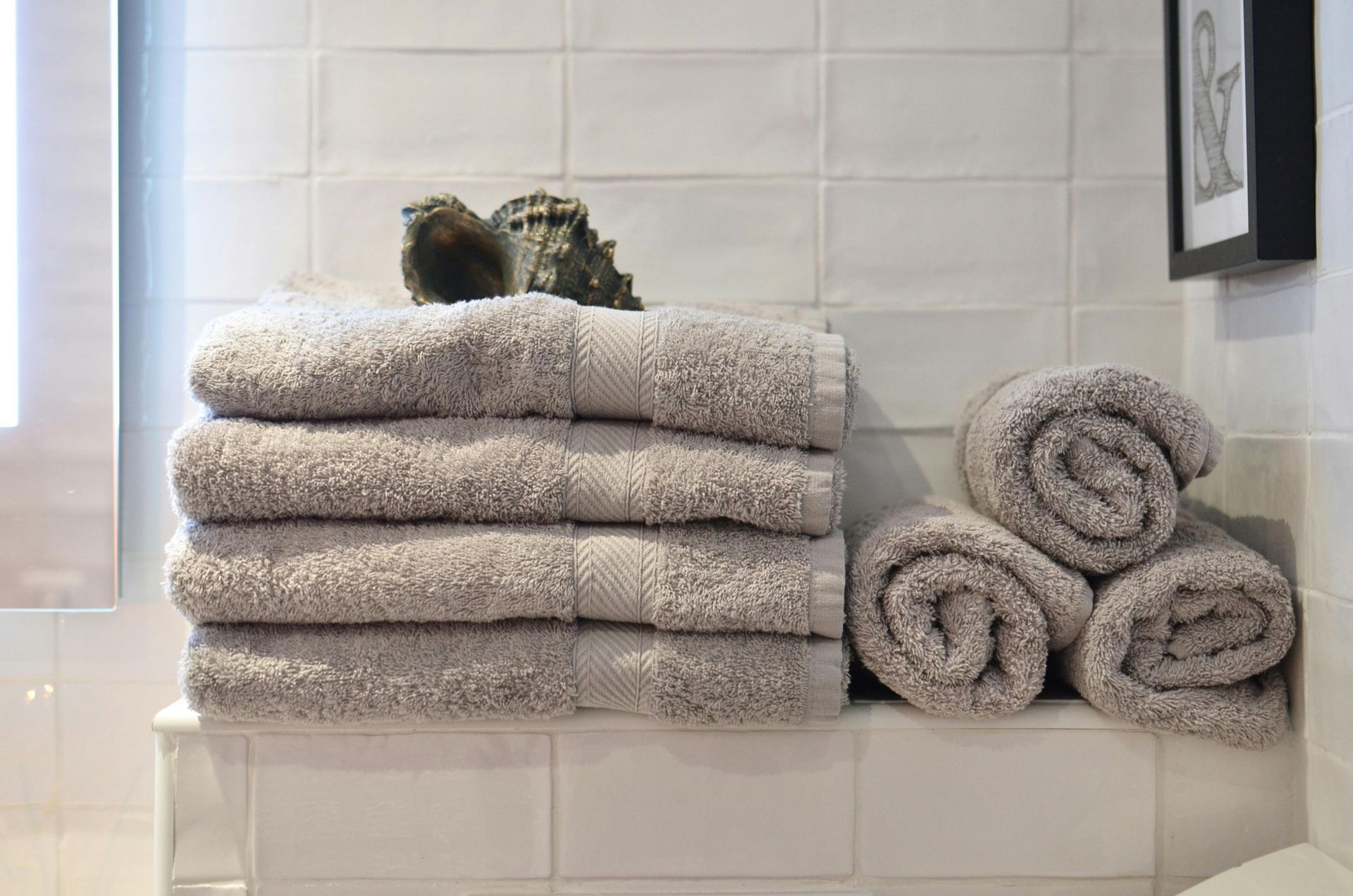 Stack of folded gray towels and rolled towels on a shelf in a bathroom.