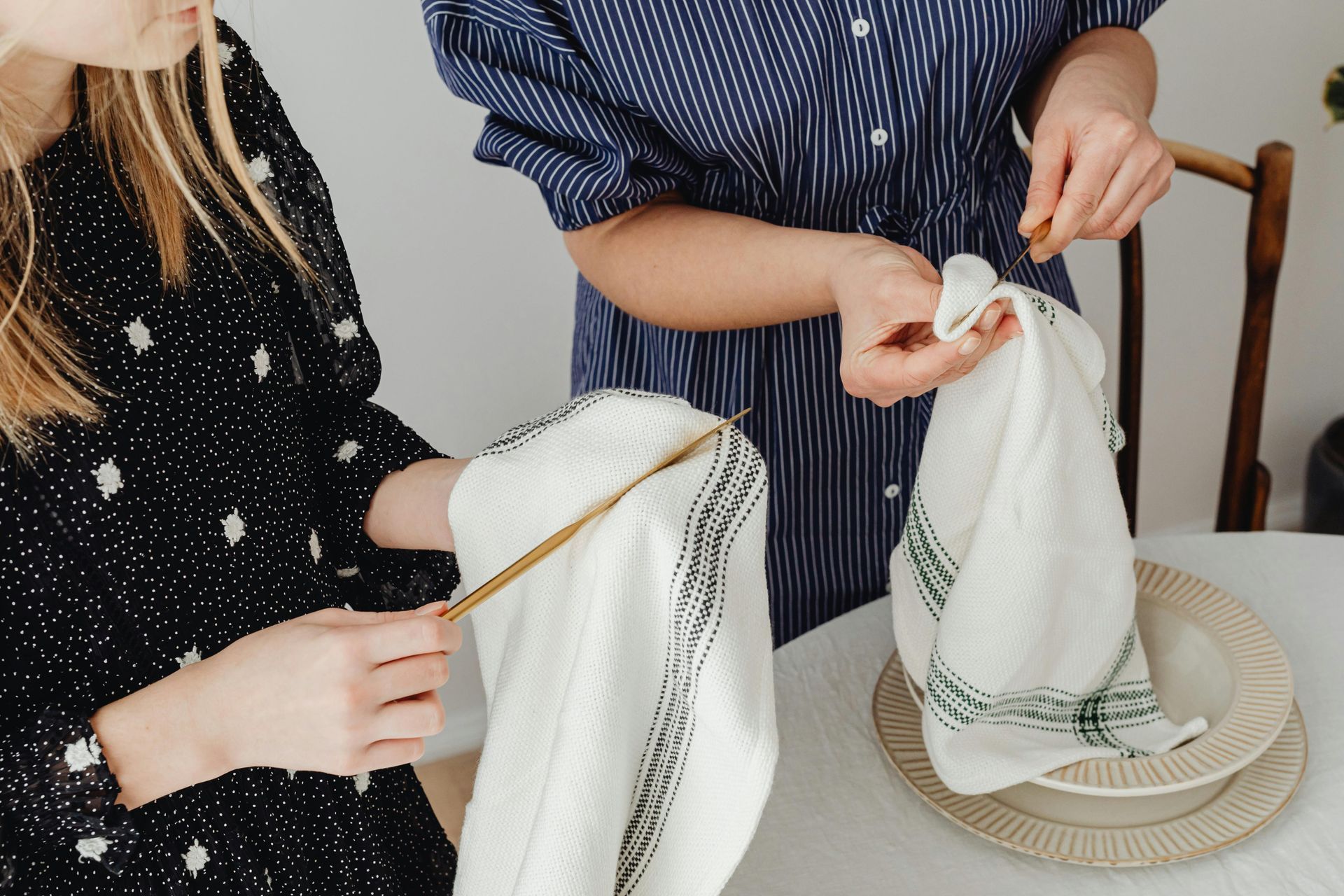 Two people folding napkins at a table, setting a dinner.