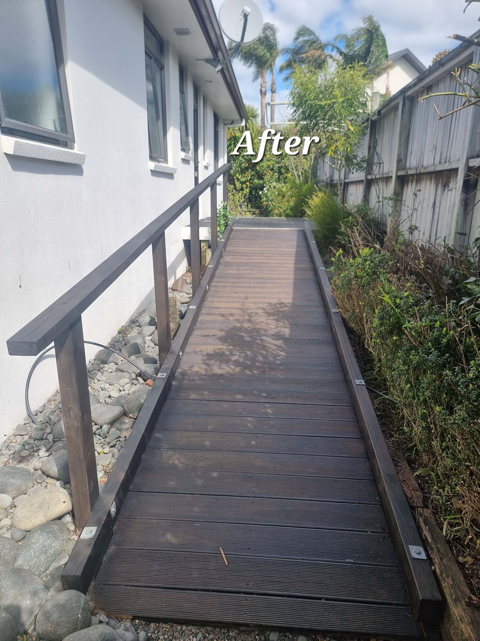 Narrow metal ramp beside a white house, leading to a fenced yard under palm trees.