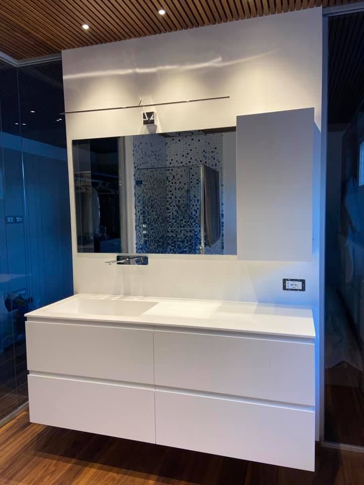 Mobile bagno moderno con ante bianche, lavabo, specchio e rivestimento a mosaico.
