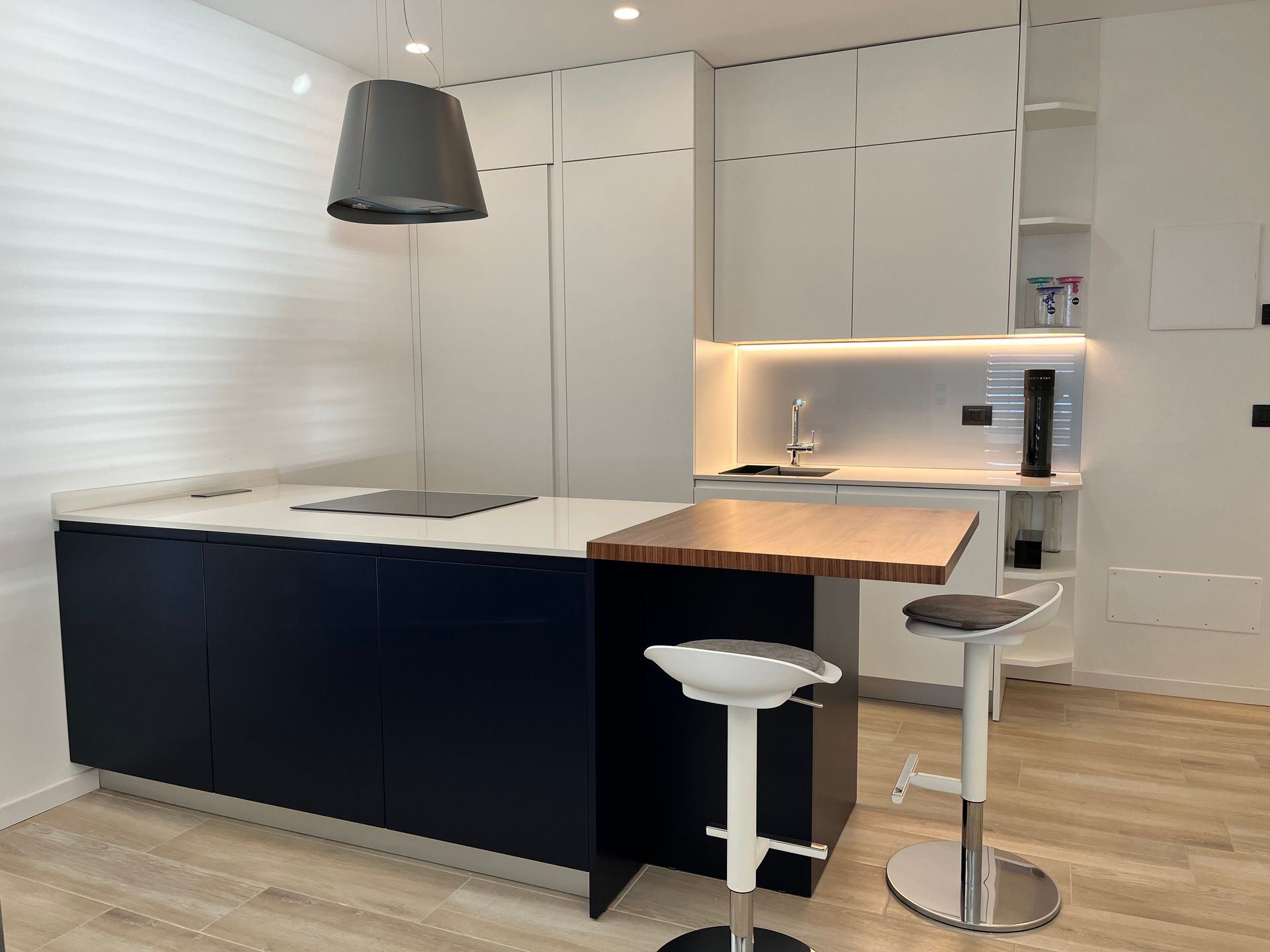 Cucina moderna con isola blu navy, mobili bianchi, piano di lavoro in legno e due sgabelli.
