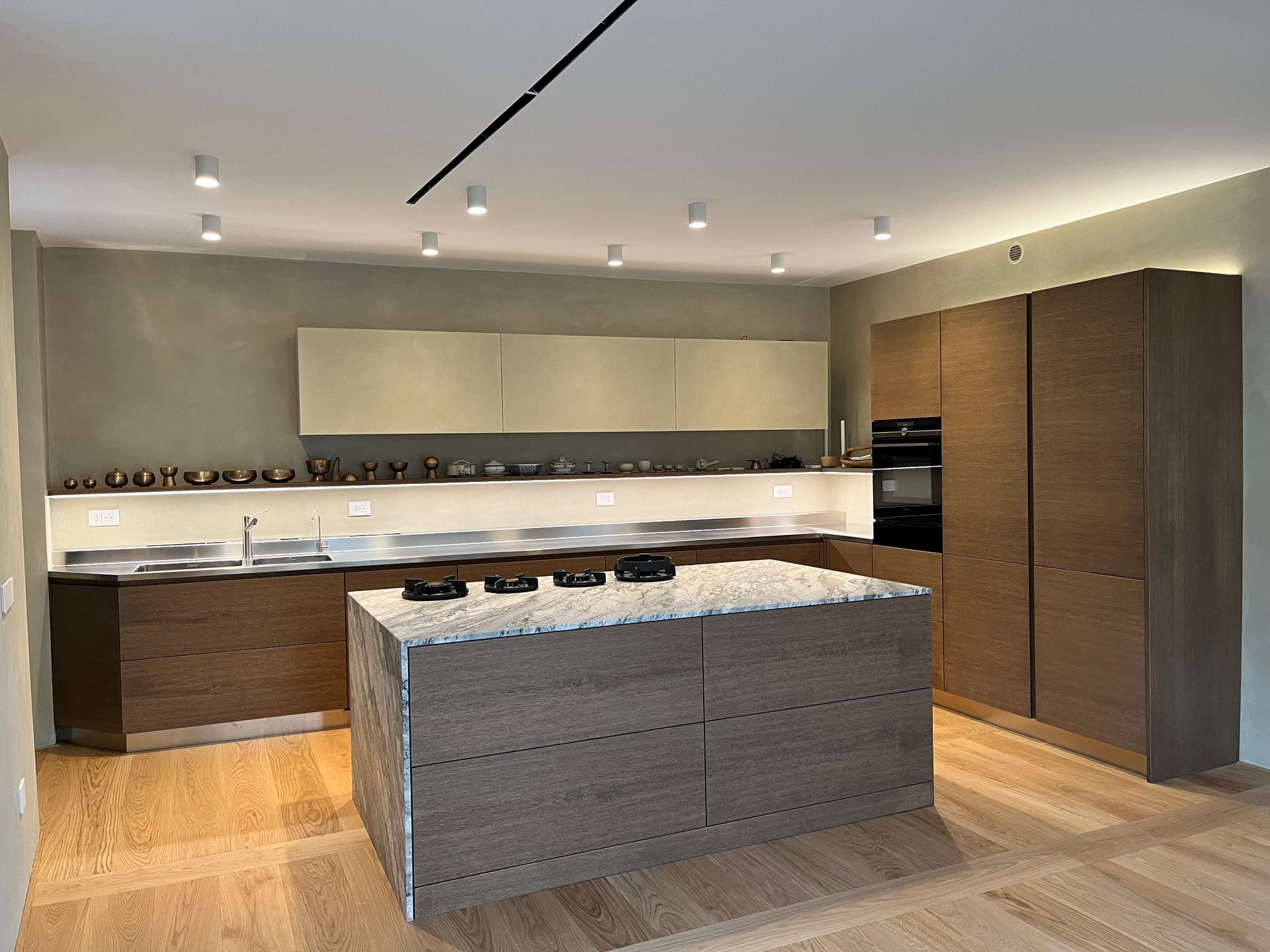 Cucina moderna con isola grigia, mobili in legno e faretti a incasso a soffitto.