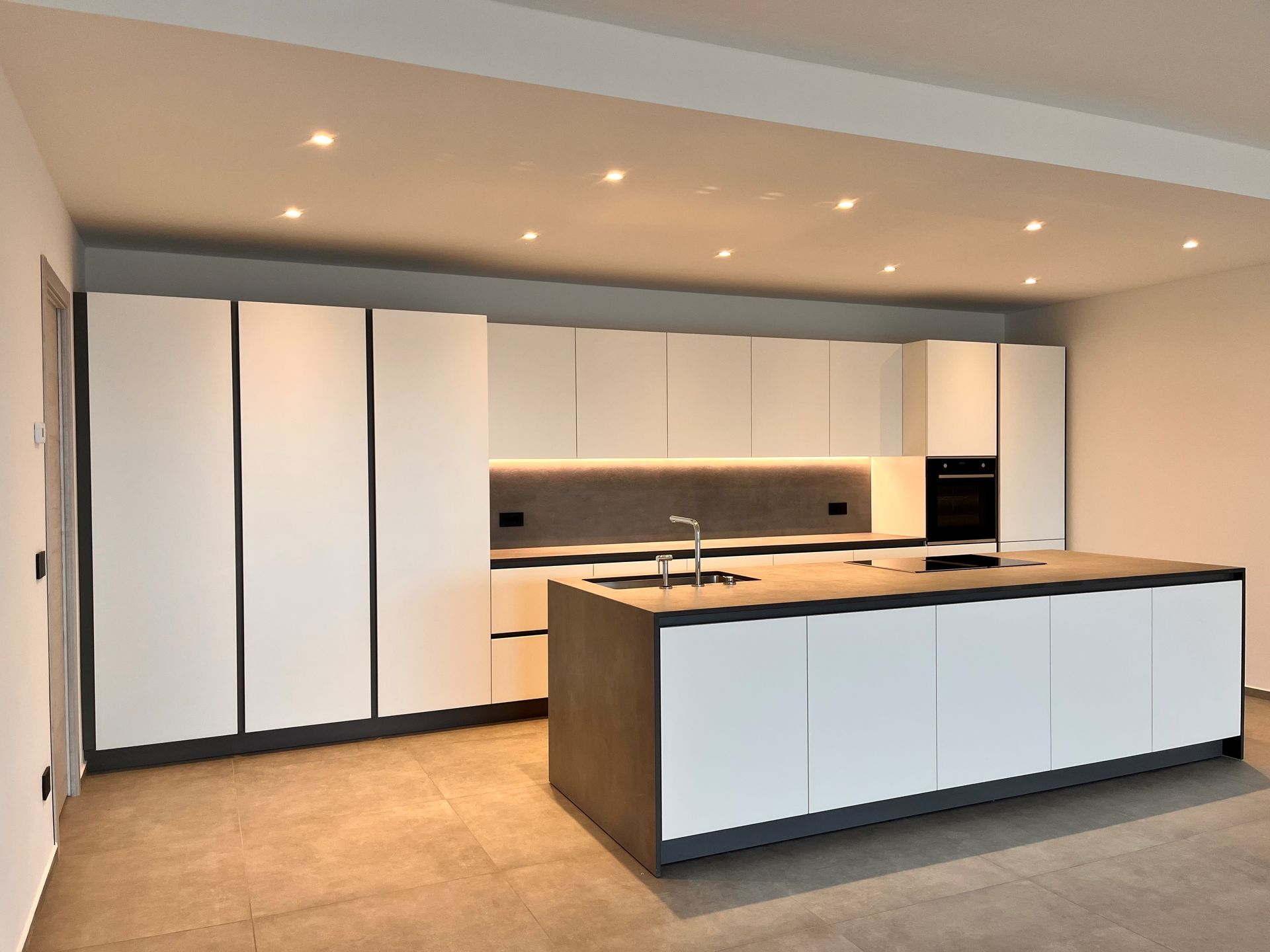 Cucina moderna con mobili bianchi, isola con piano di lavoro in legno e faretti a incasso a soffitto.