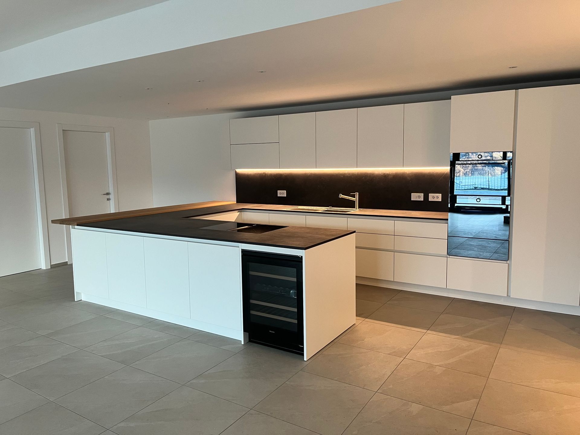 Cucina moderna vuota con mobili bianchi, paraschizzi nero, isola e pavimento piastrellato.