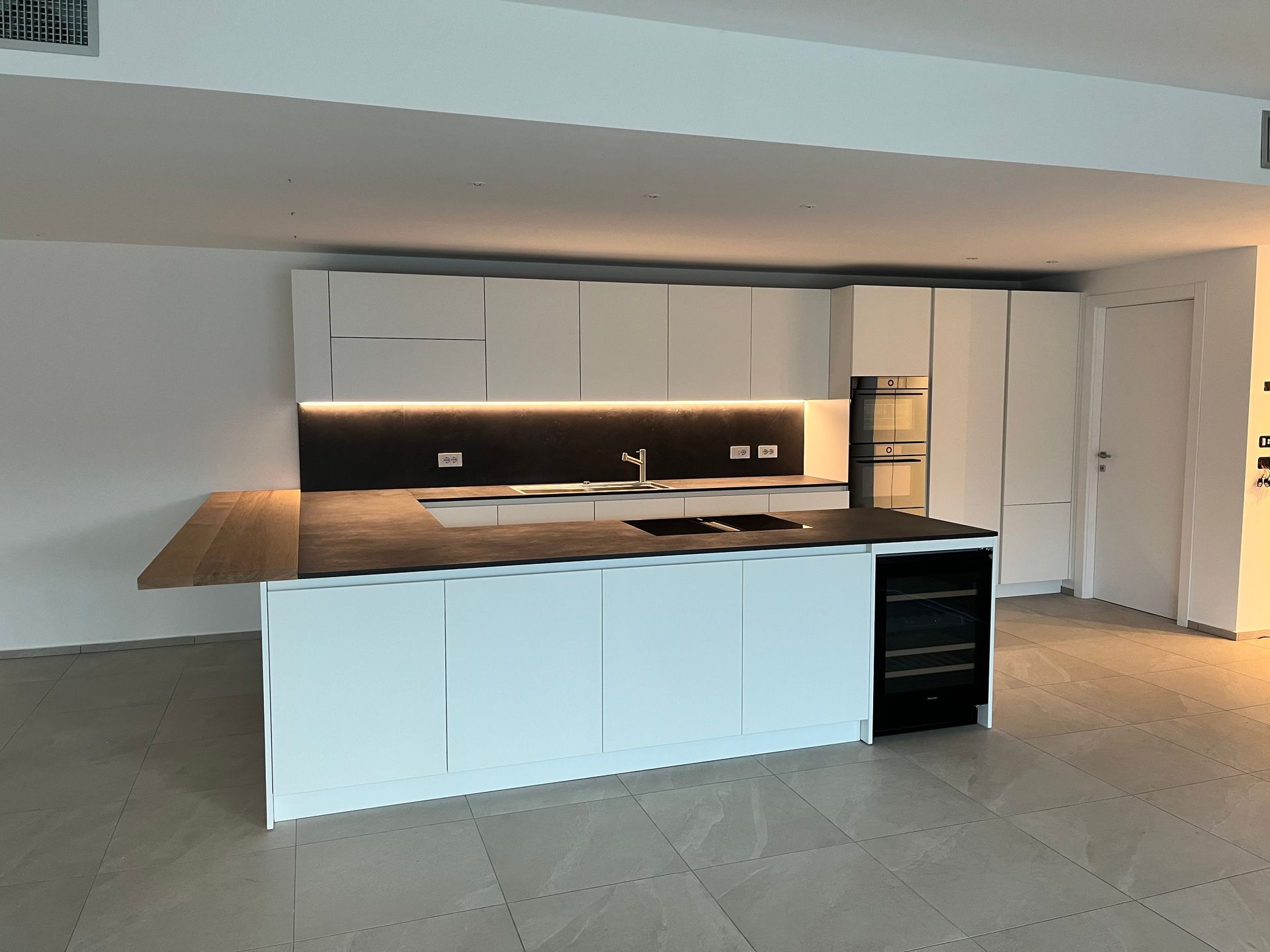 Moderna isola cucina bianca con piano di lavoro in legno e forno nero a incasso in un ampio ambiente open space.