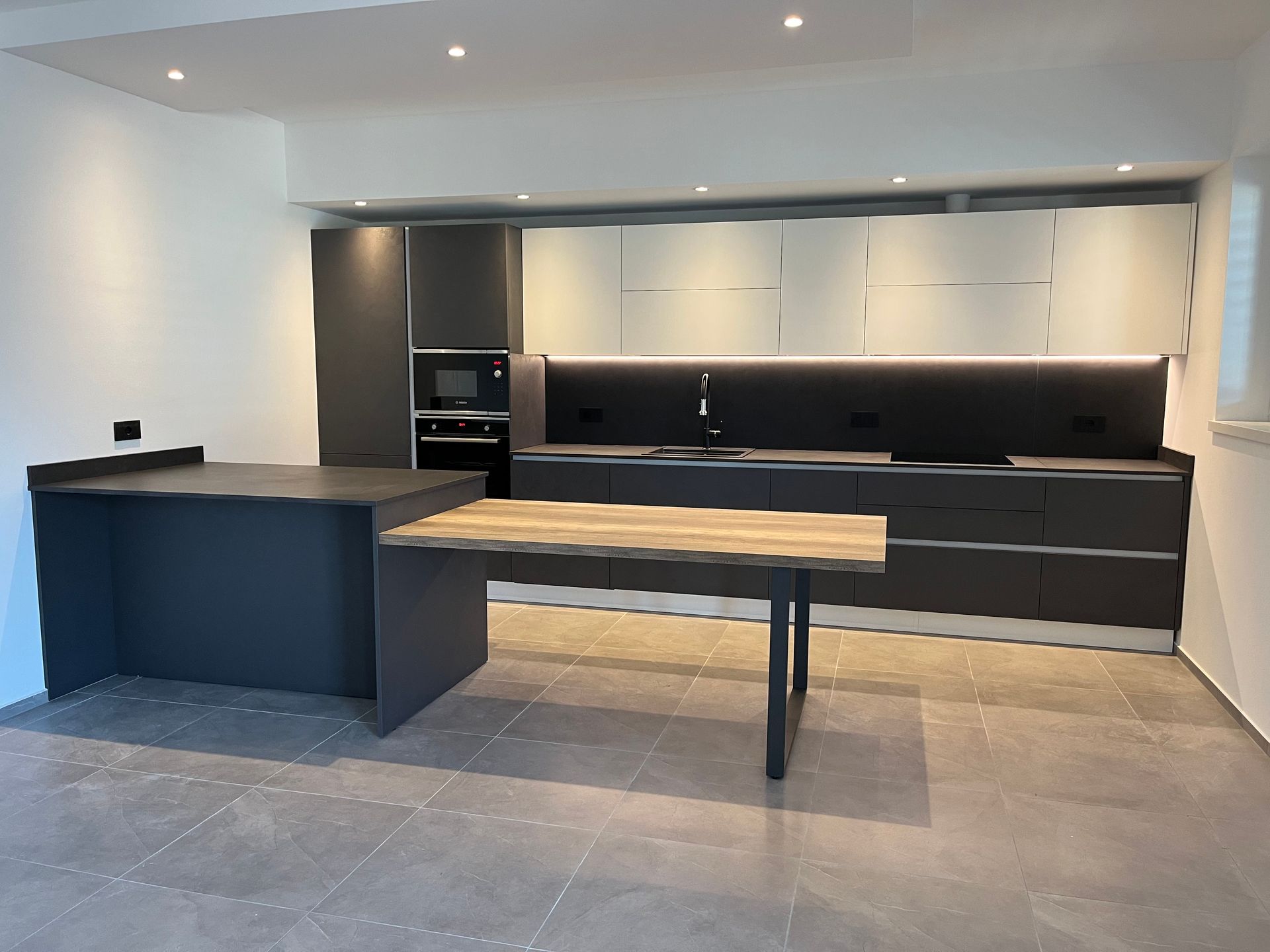 Cucina moderna con mobili scuri, isola in legno chiaro e pavimento in piastrelle grigie.