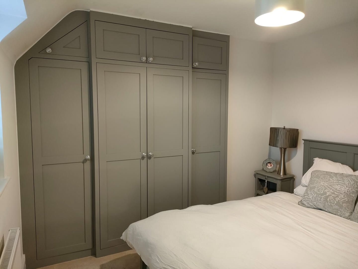 Bedroom with built-in gray wardrobe, white bed, and a small bedside table with lamp.