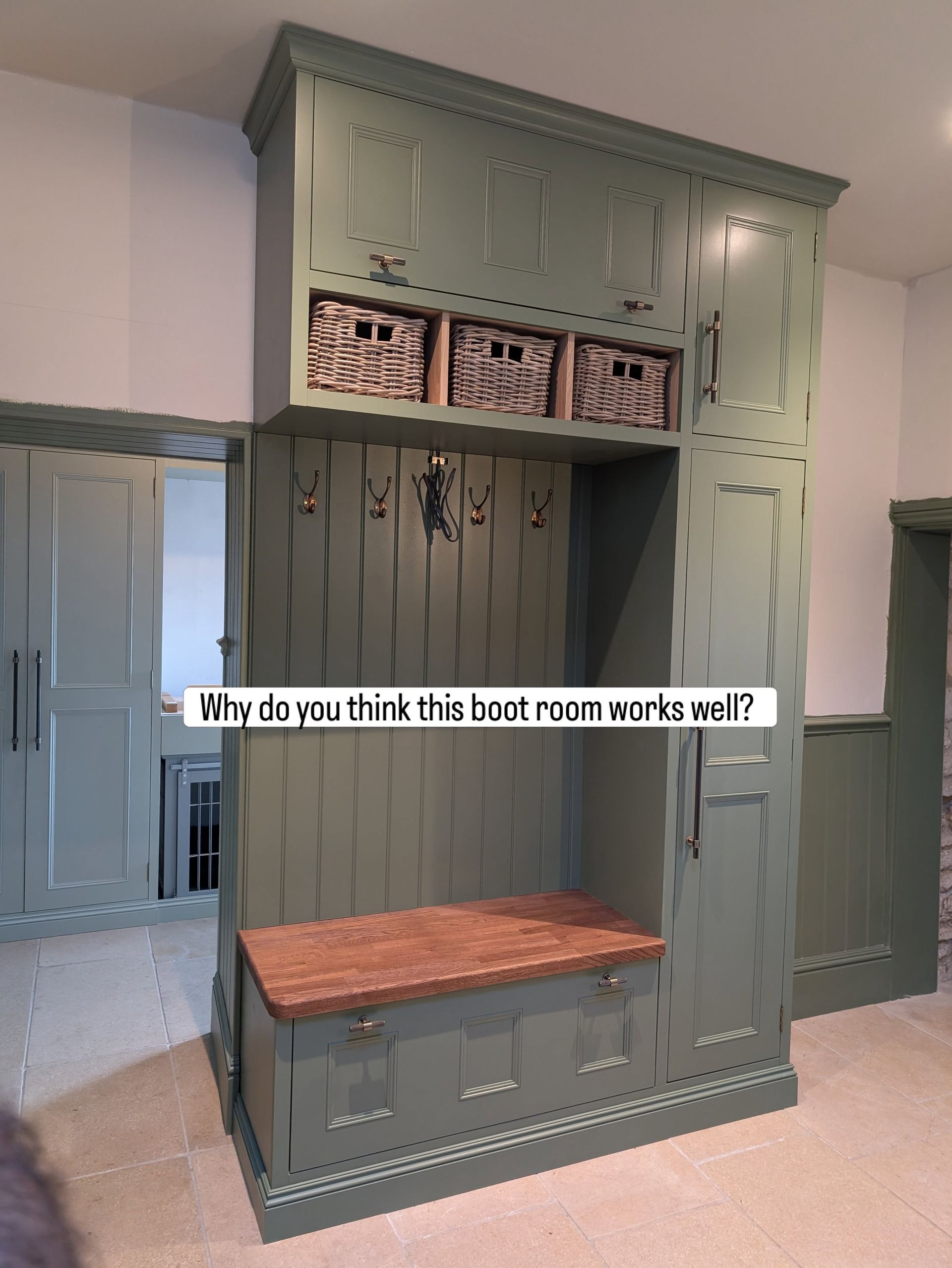 Green built-in mudroom bench with hooks, cubbies, and wicker baskets in a hallway.