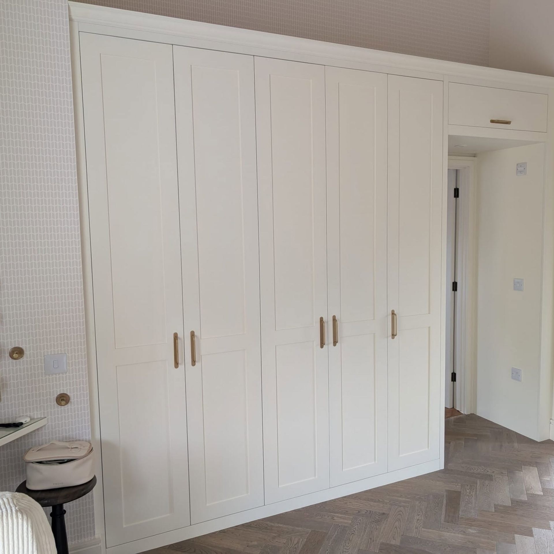 White built-in wardrobe cabinets with gold handles in a bright room with herringbone wood flooring