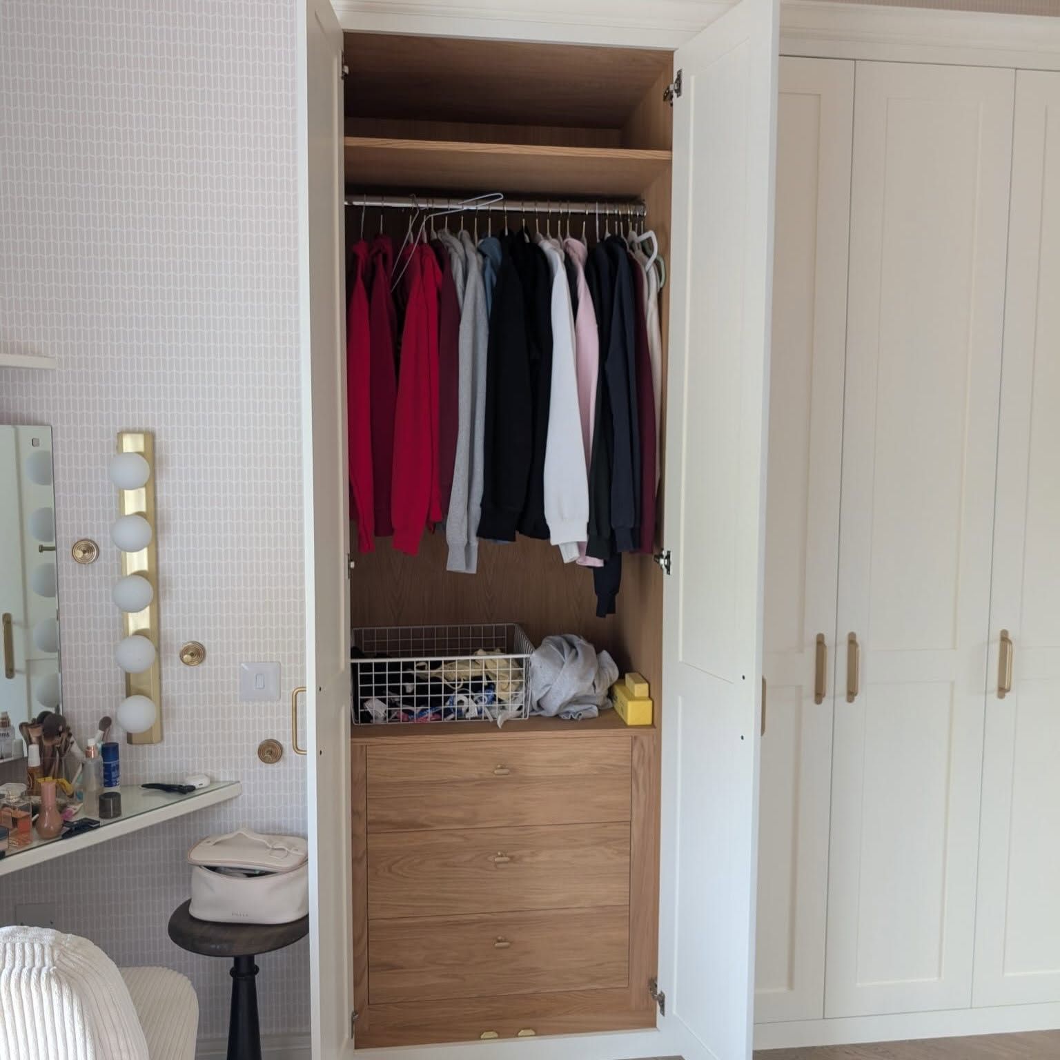 Open closet with hanging clothes and folded items in a bright bedroom.