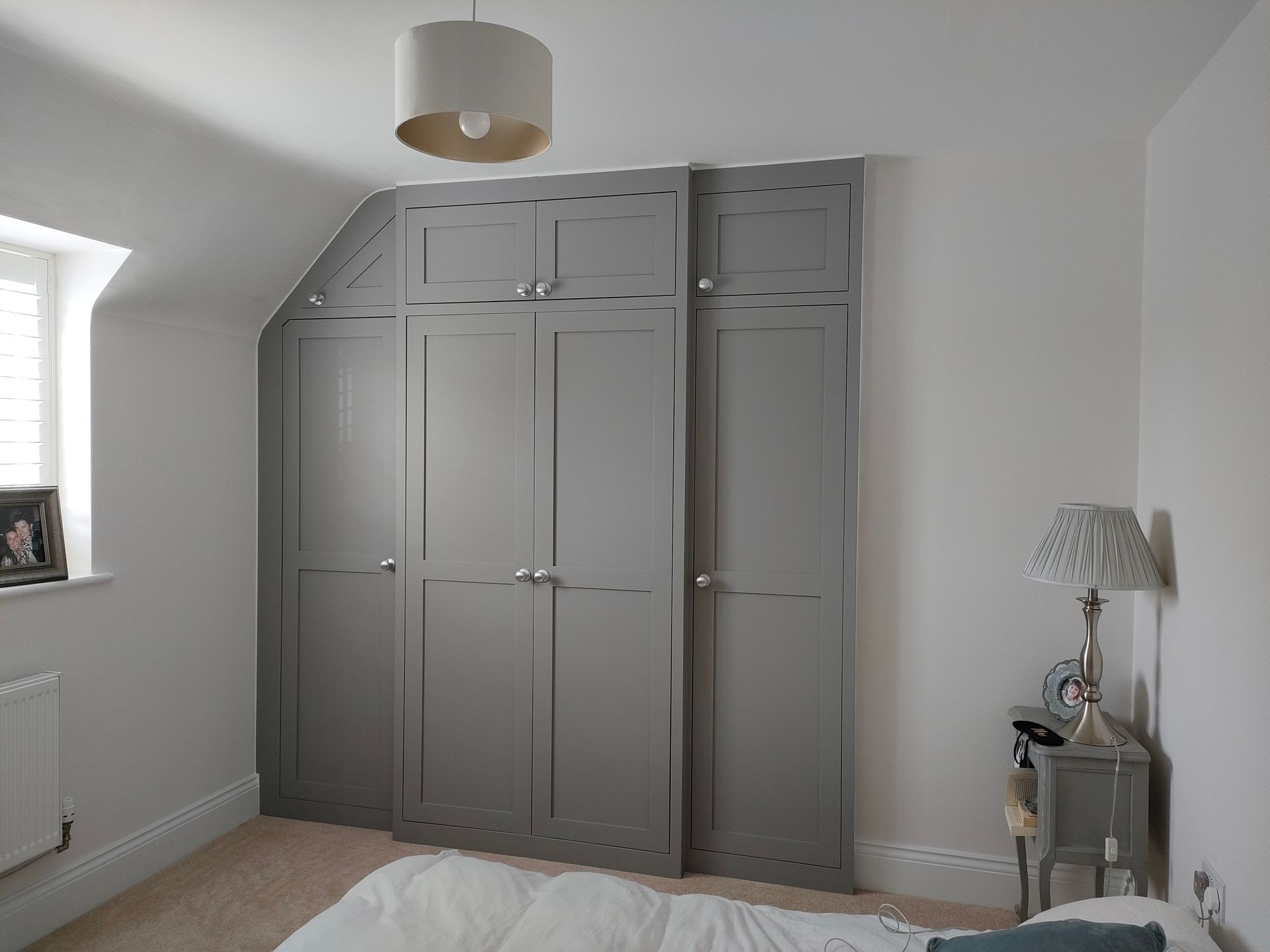 Built-in gray wardrobes in a bedroom with a small bedside table and window seat
