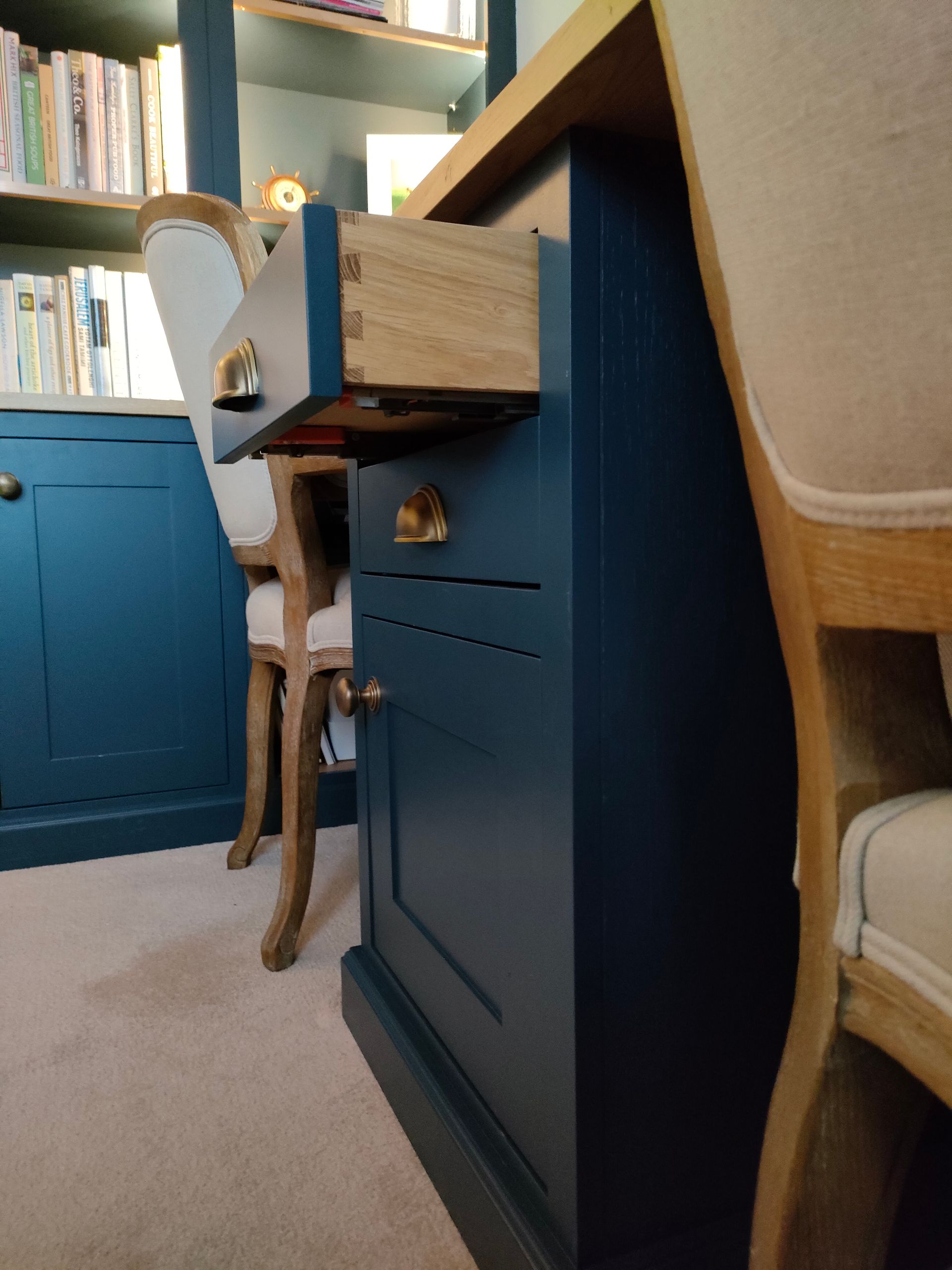 A deep blue cabinet with a pull-out wooden drawer and brass hardware, situated in a home office with a matching bookshelf.