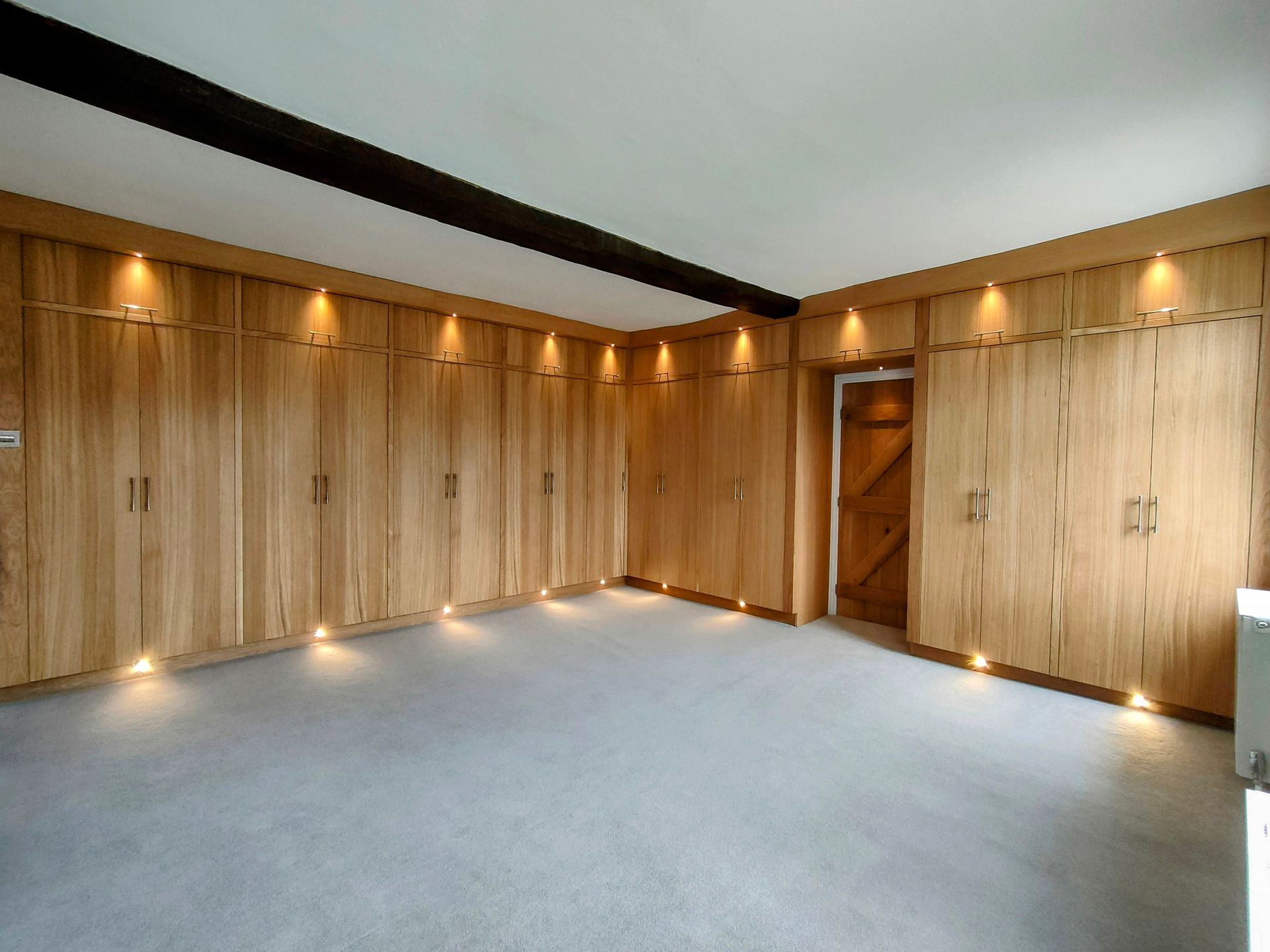 A room with wall-to-wall wood cabinetry, recessed ceiling lights, and gray carpeting.