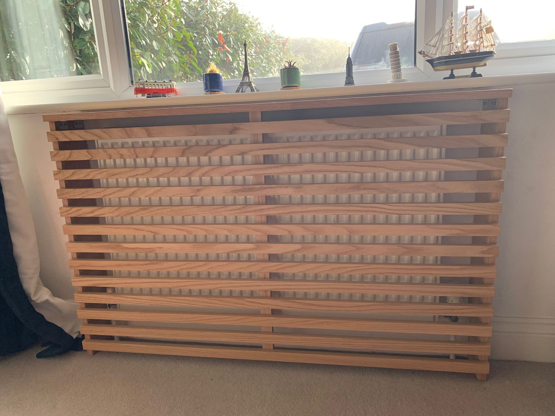 A wooden slat radiator cover sits under a window with a display of small decorative ornaments on its top ledge.